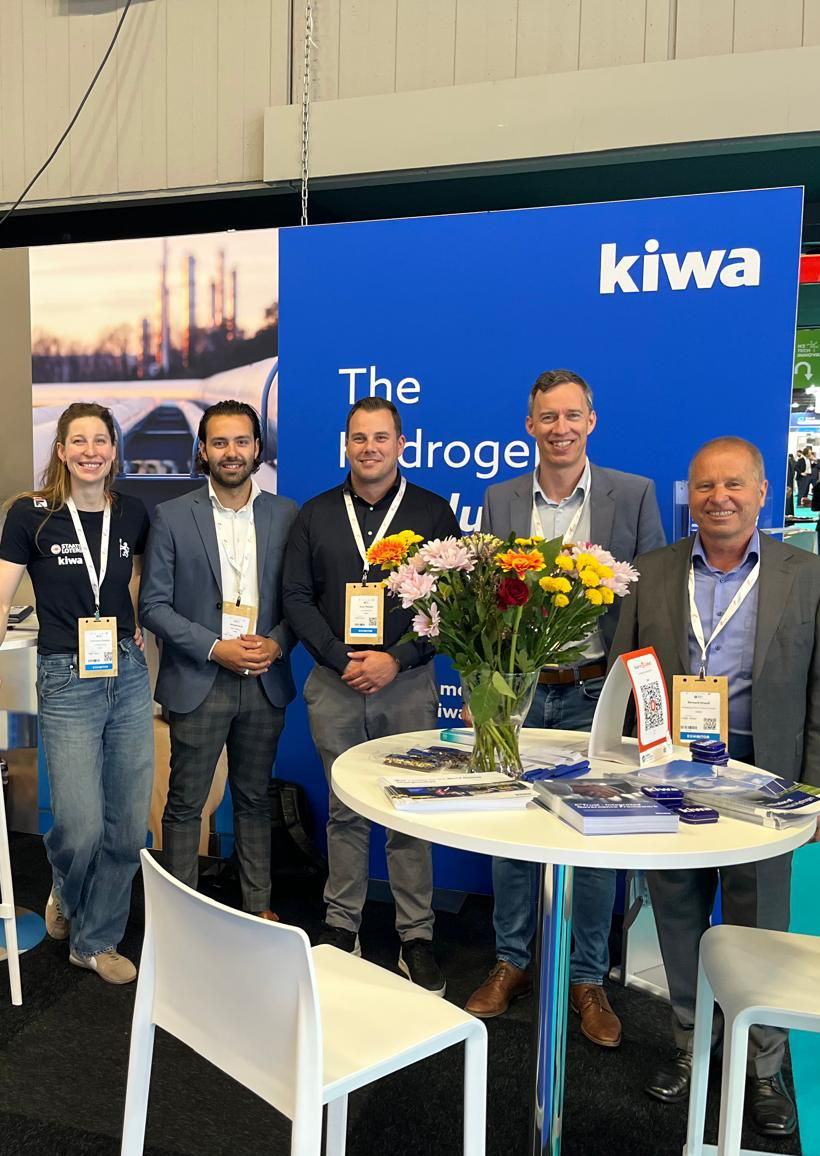 Group of five Kiwa employees standing at the World Hydrogen Summit with Kiwa promotional banners.