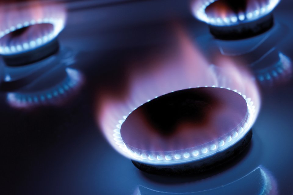 Close-up of a gas stove burner with blue flames on a black cooktop.