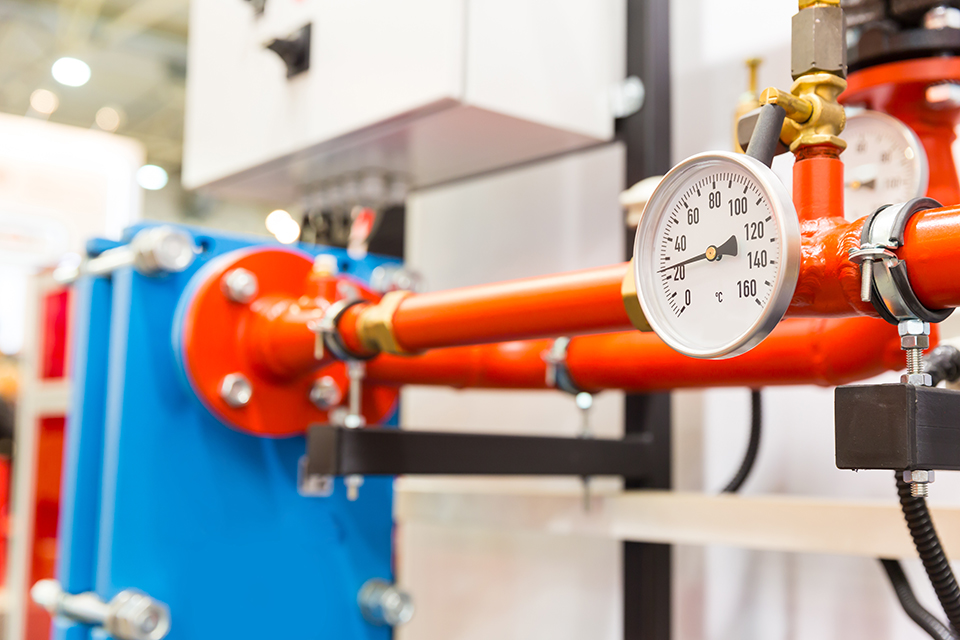 Red industrial pipe system with a pressure gauge displaying temperature in a mechanical room, indicating engineering and HVAC operations