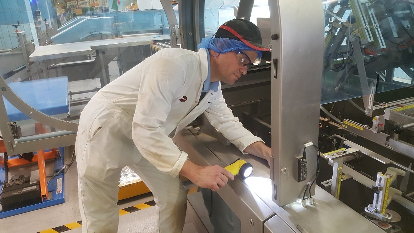 Kiwa inspectorin a white protective suit inspecting industrial machinery with a flashlight in a manufacturing facility