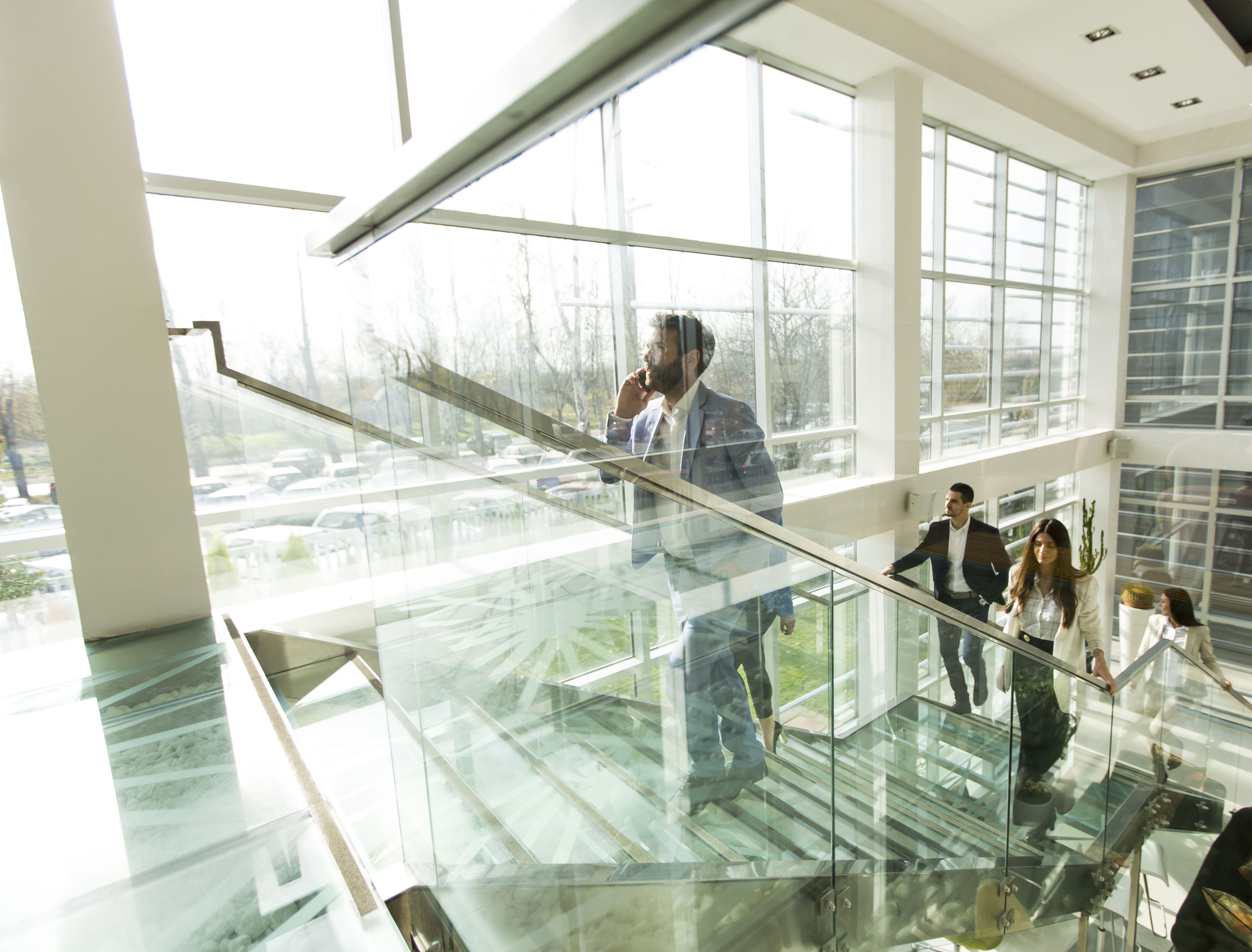Business professionals walking up a modern glass staircase in a bright office building